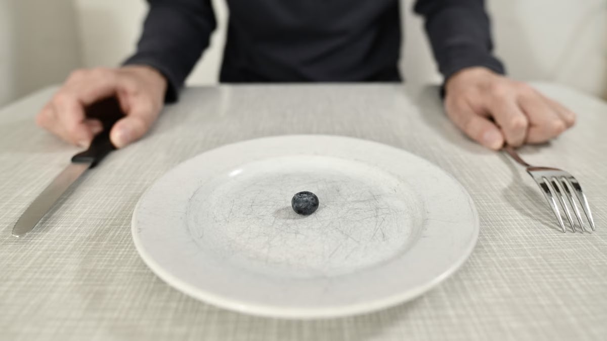A single blueberry on a scratched plate symbolizes minimalist diet and portion control.